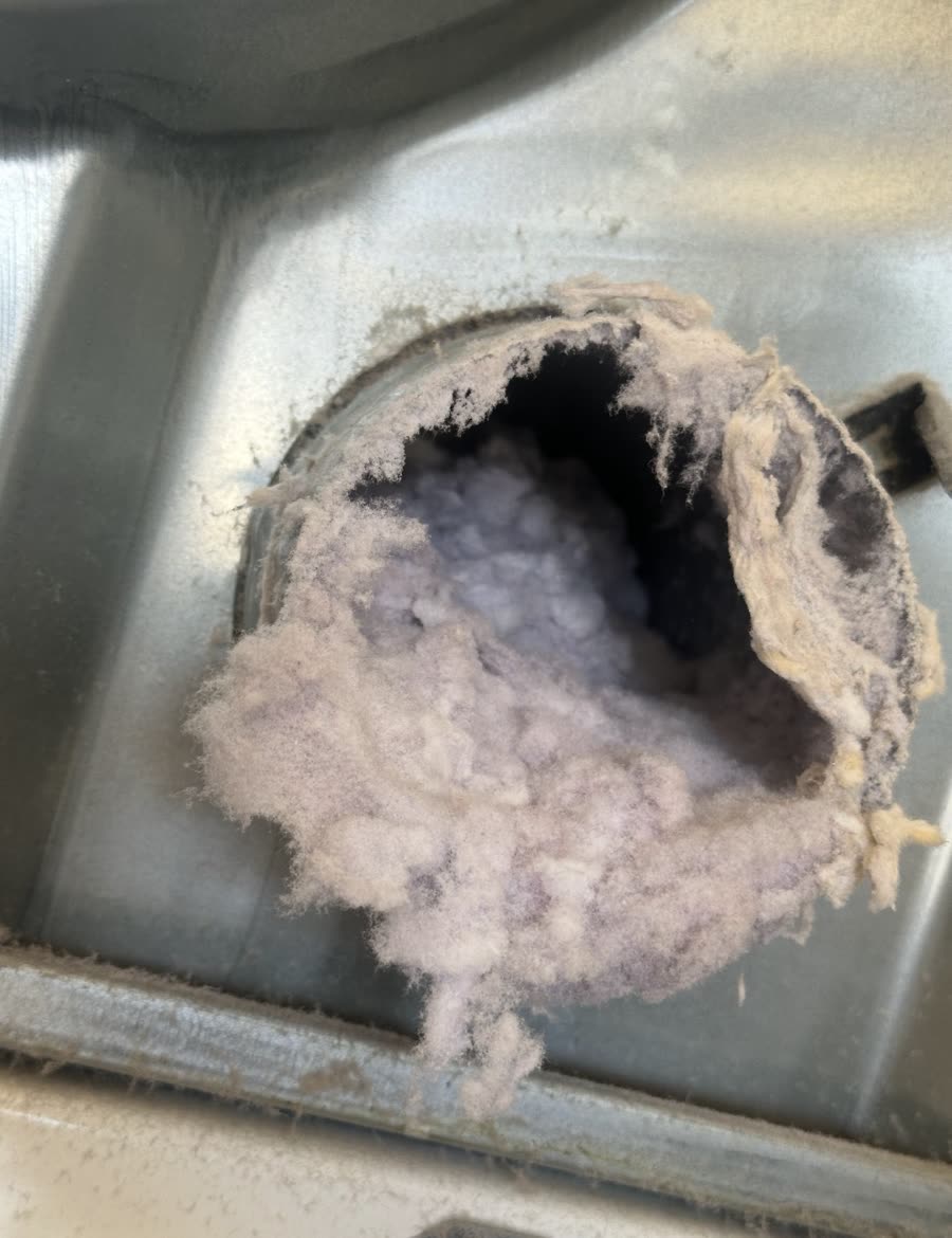 The exhaust opening on the back of a dryer, packed with lint